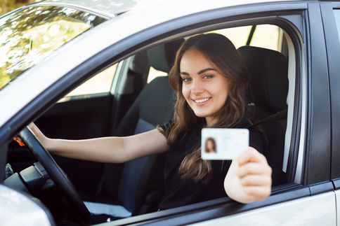 Junge Fahranfängerin am Steuer zeigt Ihren Führerschein